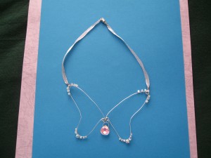 A necklace with large wire wings as the pendant decorated with crystals at the tips and a crystal drop below the body suspended on light blue ribbon.