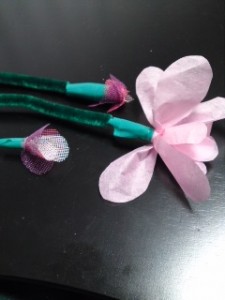 Three flowers made of pink crepe paper petals and green pipe cleaners.