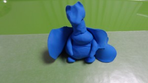 A blue clay dragon resting on its hind legs with thin wings but little detail