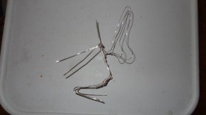 The silver wire skeleton of the faerie now complete with wings laying on a white surface.