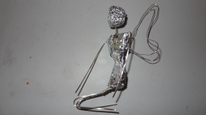 A wire skeleton, with wings, wrapped from waist to shoulders in aluminum foil with a foil ball for a head.