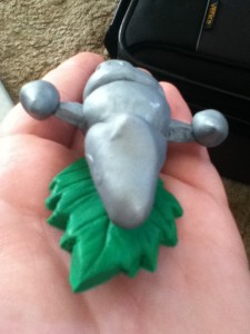 A silver polymer clay spaceship on a green clay leaf.