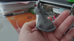 The side of the gray clay cat shows a thin tail wrapping around the body and textred fur.